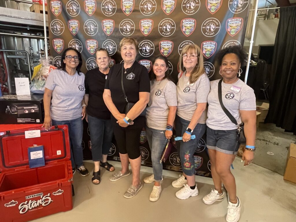 Six volunteers pose in front of a Munster Police Department K-9 Unit backdrop during the 4th Annual MPD K-9 Fundraiser at Byway Brewing.